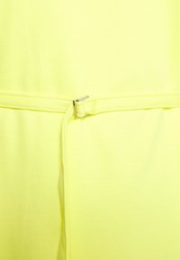 Gros plan d'une ceinture en tissu jaune vif avec une petite boucle métallique argentée qui serre le tissu à la taille.