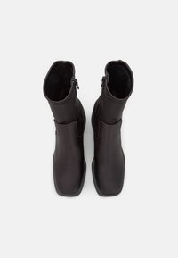 Černé kotníkové boty s hladkým koženým povrchem, čtveratou špičkou a bočními zipy, které se vyznačují minimalistickým designem a bez viditelných vzorů.