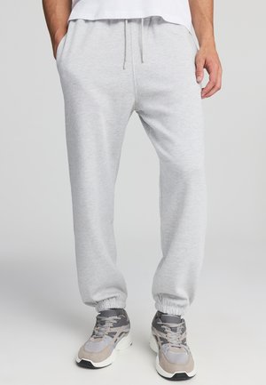 Comodi pantaloni della tuta grigi realizzati in materiale morbido, dotati di elastico in vita, polsini e tasche laterali. Abbinati a sneakers grigie e beige.