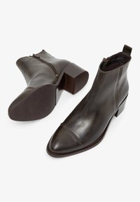 Donkerbruine leren enkellaarsjes met een puntige neus, zijrits en een stevige hak. Soepele textuur met een gestikte accént over de neus.