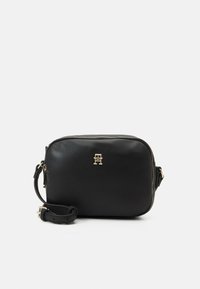 Borsa a tracolla in pelle nera con logo dorato, chiusura con zip e tracolla regolabile. Texture liscia e forma arrotondata.