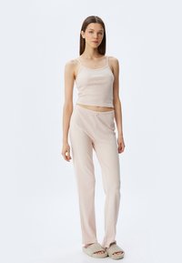 Lichtroze loungewear set met een nauwsluitend tanktop met spaghettabandjes en bijpassende ribgebreide broek, beide met subtiele textuurpatronen.