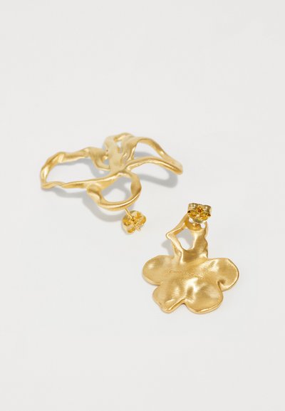 Goldfarbene Ohrringe mit einem gewellten, organischen Design und floraler Form, akzentuiert mit einem kleinen Edelstein an einem Stück. Glatte Oberfläche.