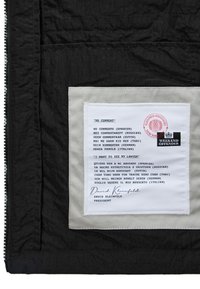 Czarna tkanina z białą naszywką przedstawiającą tłumaczenia zwrotów "Brak komentarza" oraz "Chcę zobaczyć się z moim prawnikiem" w sześciu językach, podpisana przez Davida Kleinfelda.