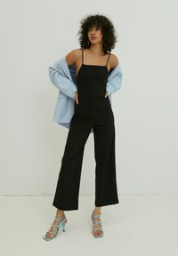 Zwarte jumpsuit met dunne bandjes, brede benen, gecombineerd met een lichtblauwe oversized blazer en blauwe hakken met bandjes.