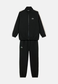 Crni trenirka od glatkog materijala. Jakna na patent s visokim ovratnikom, logotipom na prsima i uzorkovanom bočnom prugom. Hlače s elastičnim pojasom u istom uzorku.