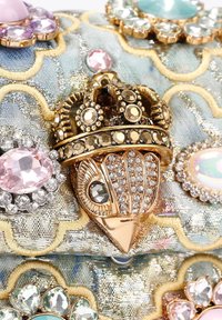 Metaliczna złota korona z cyrkoniami na tkaninie z niebiesko-żółtymi haftowanymi zawijasami, ozdobiona wielobarwnymi kamieniami.