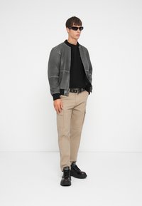 Chaqueta bomber gris con puños de canalé negros, camisa negra, pantalones cargo caqui y zapatos negros gruesos con cordones. Diseño ajustado con bolsillos.