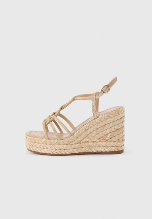 Beige wedge sandal with woven rope platform, open toe, ankle strap with buckle, and thin glittering straps across the foot.