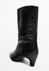 Bottine en cuir noir avec un talon effilé, texture lisse et une forme ajustée qui monte au-dessus de la cheville, avec des coutures discrètes.
