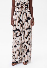 Pantalons à jambes larges en imprimé animal beige, noir et crème. Fabriqués en tissu doux avec un design fluide. Accentués d'une taille haute.