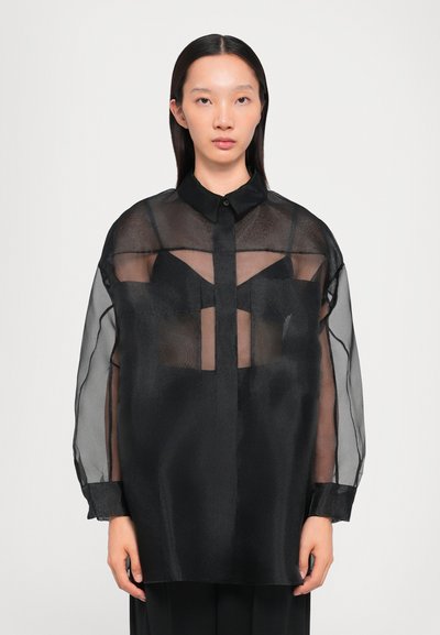 Blusa negra transparente de botones con mangas largas y transparentes, cuello negro sólido, que presenta un diseño frontal en capas y un ajuste relajado.