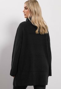 Przesadzony czarny sweter z prążkowaną teksturą, szerokimi rękawami i wysokim kołnierzem. Materiał wydaje się miękki i gruby, co zapewnia ciepło.