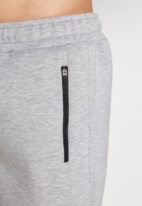 Los pantalones de chándal grises presentan un material texturizado, una cintura elástica y un bolsillo con cremallera negra en el costado para un almacenamiento seguro.