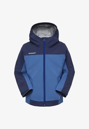 Enfant souriant aux cheveux bouclés portant une veste Mammut bleue et marine ainsi qu'un pantalon vert clair, regardant vers la droite.