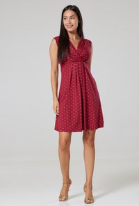 Red dress with white polka dots, sleeveless design, V-neck, pleated front, above-knee length, made from lightweight fabric.