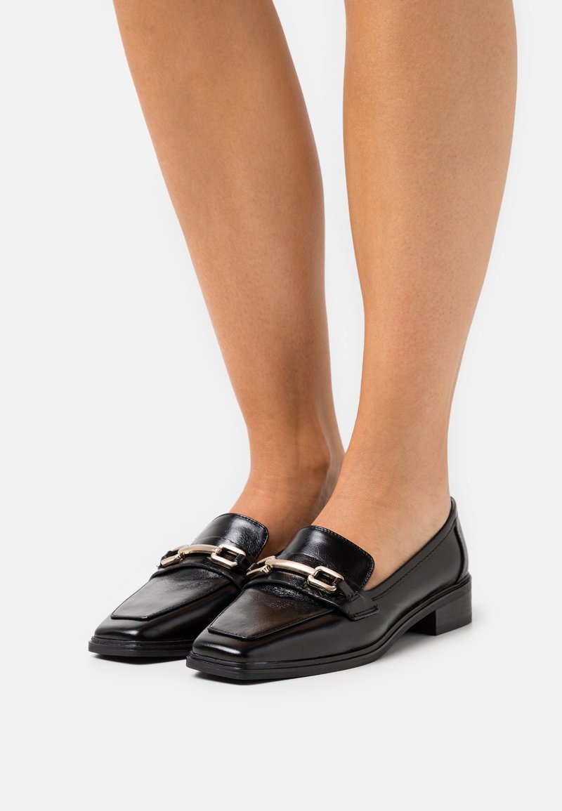 Svarta läderloafers med fyrkantig tå, som har en metallisk detalj över ovandelen och en låg blockklack för stabilitet.