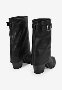 Bottes dcuir noir montantes avec un haut repli, dtail de boucle latrale et talons carrs. Texture lisse avec un design minimaliste.
