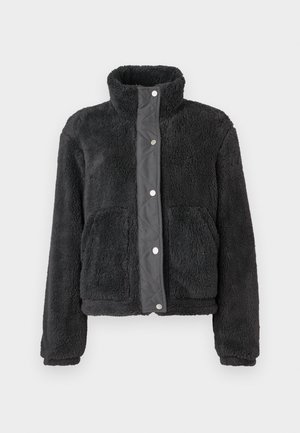 Black fleece jacket with high collar, snap button closure, and two front pockets, displayed against a plain white background.