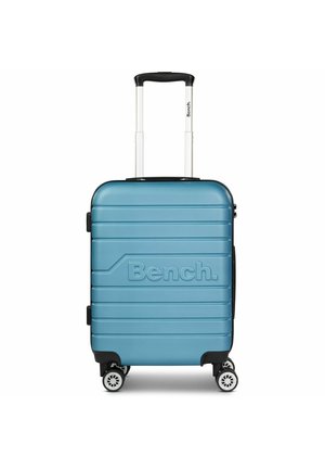 Valise rigide bleue avec logo "Bench." en relief, surface texturée, poignée rétractable et quatre roues blanches pour la mobilité.
