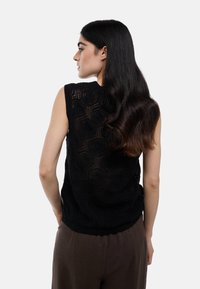 Pull sans manches noir avec un motif hexagonal, fabriqué dans une texture tricotée, présentant un ourlet côtelé et une coupe décontractée.