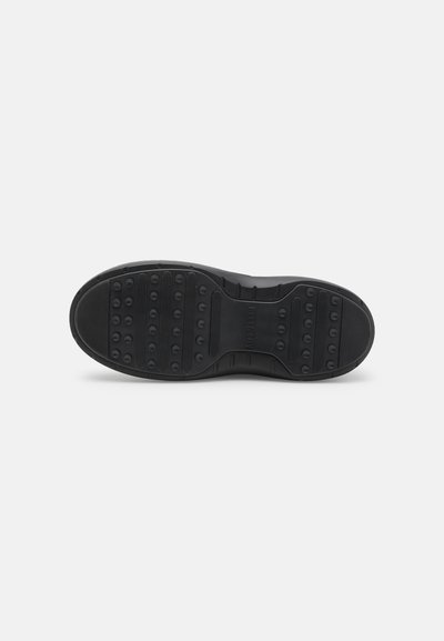 Semelle de chaussure en caoutchouc noir présentant une surface texturée avec des motifs de grip circulaires et des rainures pour une meilleure traction. Talon arrondi sans marque visible.