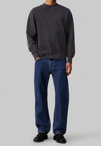 Sudadera de forro polar gris oscuro con mangas largas y puños acanalados, combinada con jeans de mezclilla azul de corte holgado y zapatos negros.