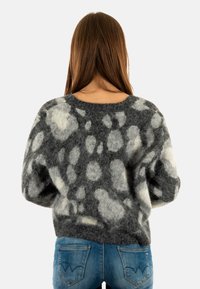 Grijze en witte fluffy trui met een zachte textuur, losse pasvorm en een gespikkeld patroon, gecombineerd met blauwe jeans. Gecurved halslijn en lange mouwen.