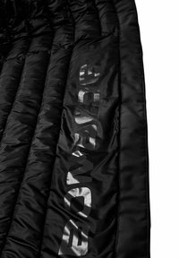 Coperta nera imbottita con texture trapuntata, caratterizzata da un logo argentato lucido su un lato, che evidenzia il suo design elegante e moderno.