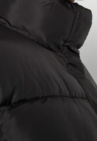 Black puffer jacket featuring a quilted design, with a smooth texture and high collar. Visible stitching and overlapping panels.