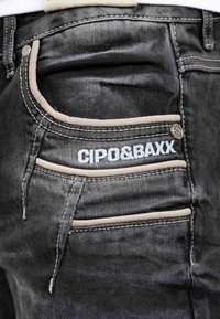 Jeans in denim neri con dettagli a contrasto in beige sulle tasche. Presentano cuciture decorative e un logo visibile sulla tasca posteriore.