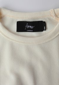 Cream-colored waffle-knit fabric with a ribbed collar. Features a black label with "former" and size "L" in white text.