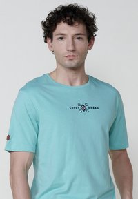 Hellblaues T-Shirt mit kurzen Ärmeln aus weicher Baumwolle, rundem Halsausschnitt und einem auf der Brust zentrierten Logo-Design.