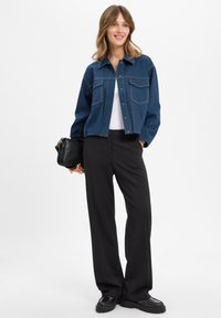 Denim jacket with a collar, two chest pockets, and contrasting stitching. Paired with high-waisted black trousers and chunky black shoes.