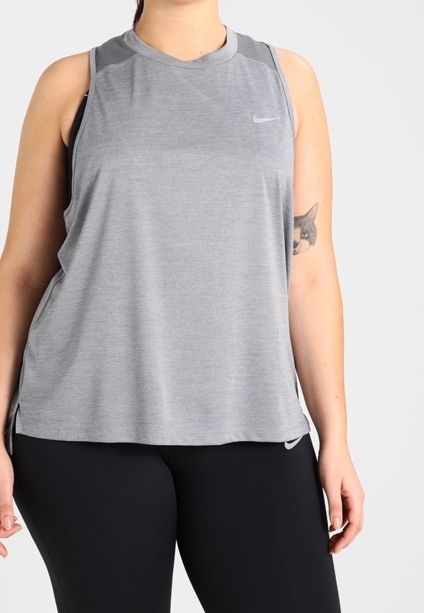 Femme portant un haut de sport gris sans manches et des leggings noirs avec un tatouage de renard visible sur son bras supérieur gauche.