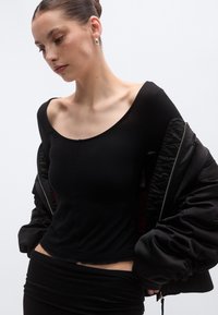 Μαύρη μπλούζα με μακριά μανίκια, στρογγυλή λαιμόκοψη και εφαρμοστή σχεδίαση, σε συνδυασμό με μαύρο μπουφάν bomber με φερμουάρ και φαρδιά μανίκια.