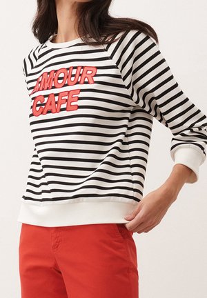 Femme portant un t-shirt à manches longues rayé noir et blanc avec un texte rouge "AMOUR CAFE" et un pantalon rouge.