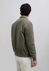 Chaqueta bomber de pana color verde oliva con puños y cintura acanalados, que presenta un cuello con solapa y una tela texturizada.