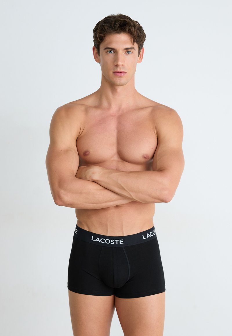 Schwarze Lacoste Boxershorts mit einem breiten elastischen Bund, auf dem der Markenname eingedruckt ist. Das Material wirkt weich und dehnbar und ist für hohen Tragekomfort konzipiert.