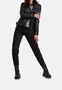 Svart lädermotorcykeljacka, grå tröja, svarta jeansbyxor och klumpiga svarta ankelboots; visar en lager-på-lager-look med en texturerad finish.