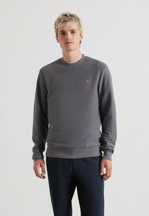 Grau strukturierter Pullover mit rundem Ausschnitt, gerippten Bündchen und Saum. Kleines oranges Logo auf der linken Brust. Kombiniert mit dunklen Hosen.