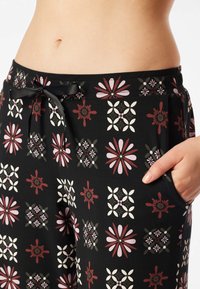 Pantaloni neri con motivi floreali in rosso, rosa e bianco. Presentano una vita elastica con fiocco e tasche laterali.