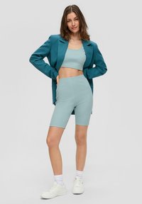 Teal blazer over een bijpassende korte tanktop en fietsshorts, allemaal in een textuurstof. Gestyled met witte sneakers en geribde sokken.