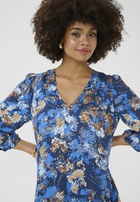 Bloemrijk patroon jurk in blauw met tinten bruin en crème, met een V-hals, pofmouwen en zachte stof.
