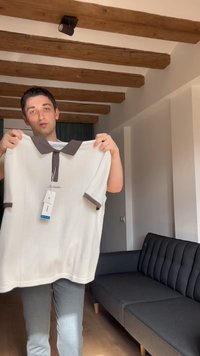 Homme debout à l'intérieur tenant un polo blanc avec un col et des bords de manches foncés, une étiquette suspendue au col.