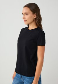 T-shirt nera a maniche corte con scollo rotondo. Tessuto liscio con un design aderente, abbinato a jeans di denim blu.