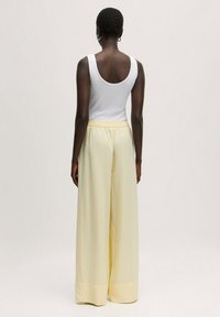 Brede, lichte broek van zacht gele stof met een elastische taille. Gecombineerd met een aansluitend wit tanktop. Een gladde textuur en een casual ontwerp.