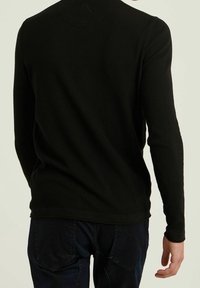 Czarna dzianinowa koszula z długim rękawem o fakturowanej tkaninie, dopasowanym kroju i okrągłym dekolcie; zestawiona z ciemnymi spodniami dżinsowymi.