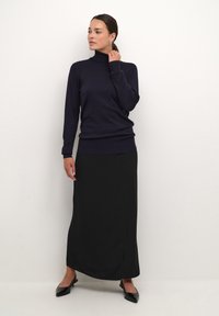 Marineblauwe coltrui van zachte brei, gecombineerd met een vloeiende zwarte maxi-rok. Zwarte puntige instappers maken de outfit compleet. Eenvoudig, stijlvol ontwerp.