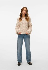 Maglione a maglia grossa in morbido crema con sfumature multicolori; presenta un motivo a trecce, maniche larghe e una vestibilità rilassata. Abbinato a jeans a gamba larga azzurri.